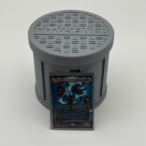 May include: A gray, cylindrical container with a lid featuring the word "SEWER" and other text. A trading card with the title "Heroes in a Half Shell" is in front of the container. The card features four cartoon turtles.