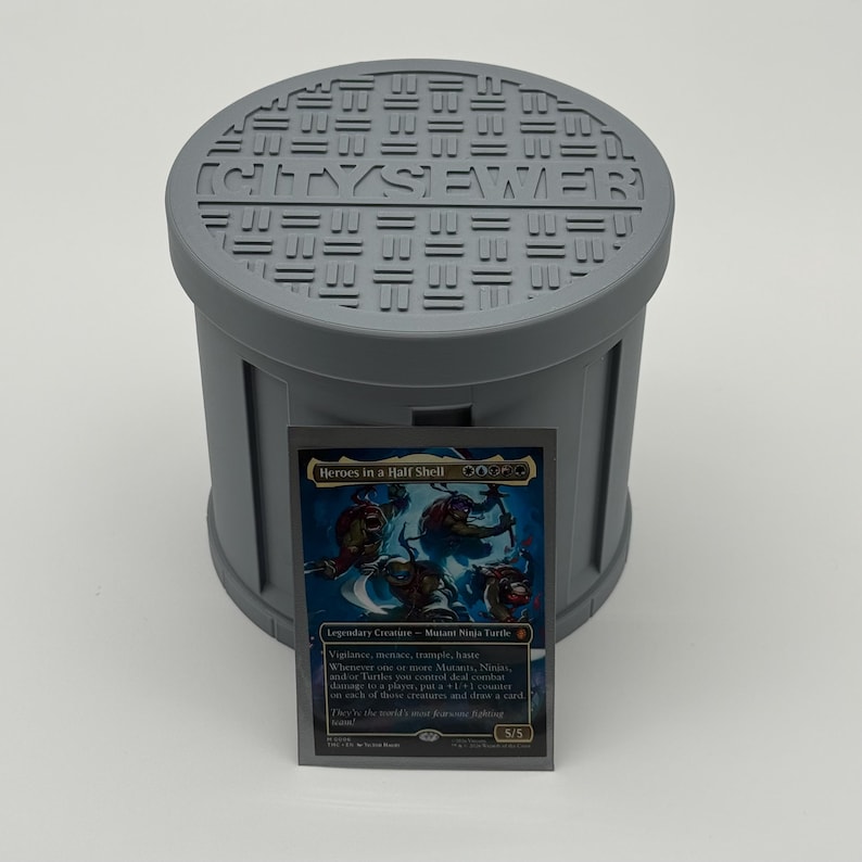 May include: A gray, cylindrical container with a lid featuring the word "SEWER" and other text. A trading card with the title "Heroes in a Half Shell" is in front of the container. The card features four cartoon turtles.