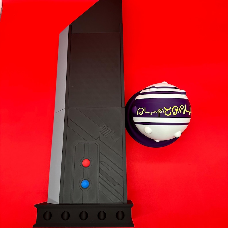 May include: A black and gray obelisk-shaped object with red and blue buttons, and a spherical object with white and purple stripes and gold text, set against a red background.