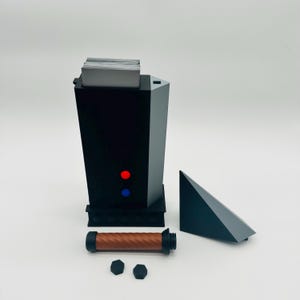 May include: A black and gray geometric device with red and blue lights, a brown handle, and a gray triangular piece. The device has a slot at the top holding a stack of white cards. Two black hexagonal pieces are also present.
