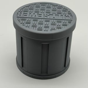 May include: A cylindrical, gray container with a removable lid. The lid features a repeating geometric pattern and text. The container's body has vertical rectangular indentations. The overall design suggests a storage or decorative item.