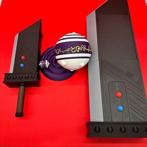 May include: A black and gray sword, a purple and white sphere with text, and a gray and black structure are displayed on a red surface. The sword has a brown handle and red and blue accents. The sphere has white and purple stripes.