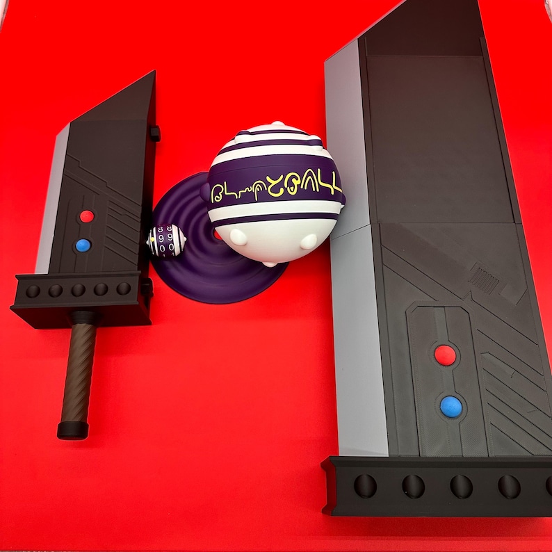 May include: A black and gray sword, a purple and white sphere with text, and a gray and black structure are displayed on a red surface. The sword has a brown handle and red and blue accents. The sphere has white and purple stripes.