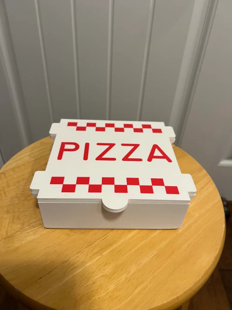 Op de afbeelding: Witte kartonnen pizzadoos met rode geruite rand en het woord "PIZZA" in rode letters.