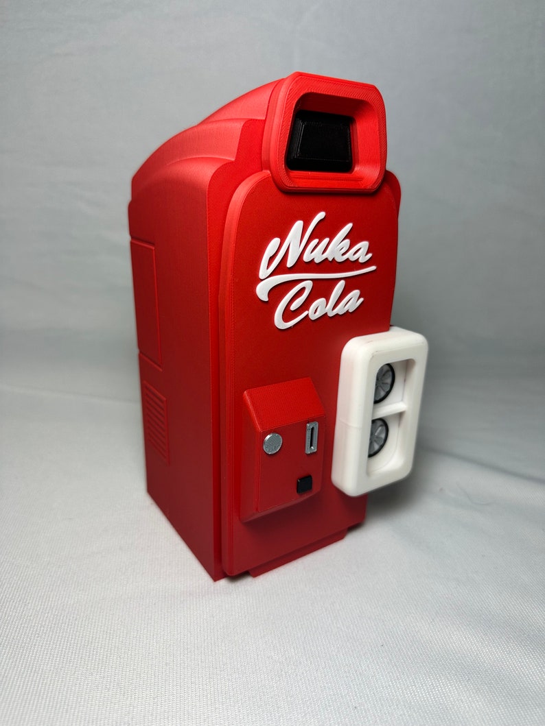 May include: Red and white 3D printed Nuka Cola vending machine with a white coin slot and a white panel on the side with two round buttons.