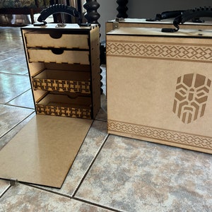 Op de afbeelding: Twee houten opbergdozen met een decoratief ontwerp. Een doos heeft een scharnierend deksel en drie laden. De andere doos heeft een scharnierend deksel en een afbeelding van een gezicht met een baard.