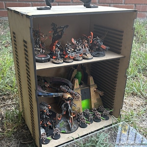 May include: A wooden box with a handle, containing a collection of miniature figures painted in black, orange, and green. The figures are arranged on a shelf inside the box, with a clear plastic lid on top.