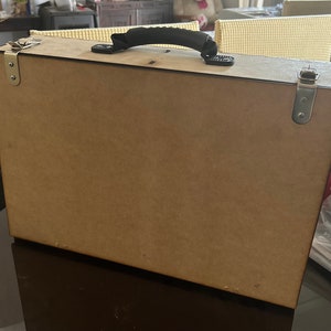 Op de afbeelding: Een bruine houten kist met een zwarte handgreep en zilveren sluitingen. De kist is gesloten en staat op een donker oppervlak.