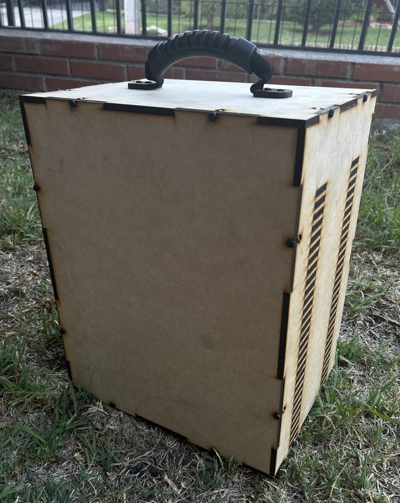 May include: A wooden box with a black plastic handle. The box has a wood grain finish and is made of plywood. The box has a series of slots on one side.