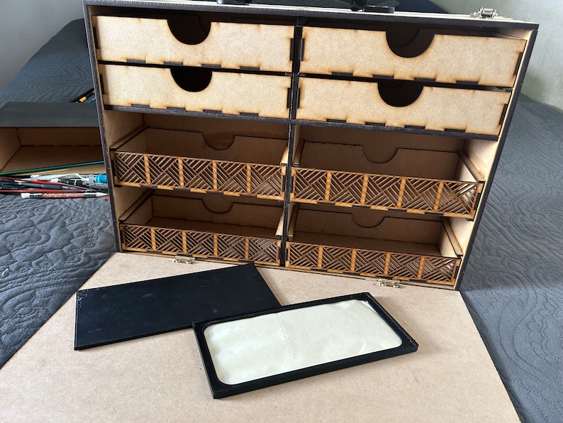 Op de afbeelding: Een houten opbergdoos met meerdere laden en vakken. De doos is open en de laden zijn leeg. De doos heeft een zwarte rand en een zwarte handgreep.