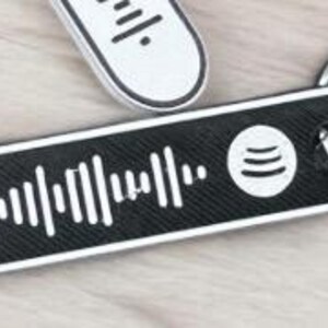 K&ouml;nnte beinhalten: Ein schwarz-wei&szlig;er Spotify-Code-Schl&uuml;sselanh&auml;nger mit einem silbernen Schl&uuml;sselring. Der Schl&uuml;sselanh&auml;nger hat eine rechteckige Form mit abgerundeten Kanten. Das Spotify-Logo ist auf der rechten Seite des Schl&uuml;sselanh&auml;ngers zu sehen.