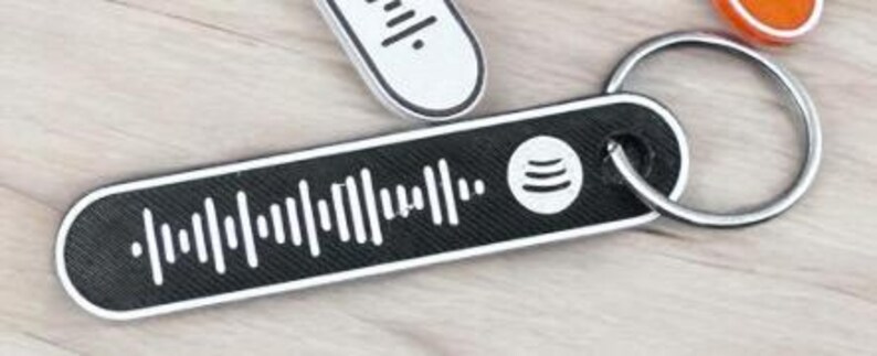 K&ouml;nnte beinhalten: Ein schwarz-wei&szlig;er Spotify-Code-Schl&uuml;sselanh&auml;nger mit einem silbernen Schl&uuml;sselring. Der Schl&uuml;sselanh&auml;nger hat eine rechteckige Form mit abgerundeten Kanten. Das Spotify-Logo ist auf der rechten Seite des Schl&uuml;sselanh&auml;ngers zu sehen.