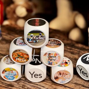 May include: A set of eight white dice with different images and text on each side. The dice are stacked in a pyramid shape. The text on the dice includes "Go Karting", "Board Games", "Dance Party", "Pizza", "Water Play", "Puzzles", "Yes", and "No".