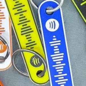 K&ouml;nnte beinhalten: Schl&uuml;sselanh&auml;nger in verschiedenen Farben, darunter Gelb und Blau, jeweils mit einem einzigartigen Audio-Wellenform-Design und einem Metall-Schl&uuml;sselring. Der blaue Schl&uuml;sselanh&auml;nger zeigt ein wei&szlig;es Spotify-Logo. Die Schl&uuml;sselanh&auml;nger sind rechteckig mit abgerundeten Kanten.