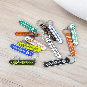 K&ouml;nnte beinhalten: Eine Sammlung farbenfroher Schl&uuml;sselanh&auml;nger mit Spotify-Code-Design. Die Schl&uuml;sselanh&auml;nger sind in verschiedenen Farben erh&auml;ltlich, darunter Gr&uuml;n, Orange, Blau, Gelb, Schwarz und Wei&szlig;. Jeder Schl&uuml;sselanh&auml;nger hat einen silbernen Ring zum Befestigen von Schl&uuml;sseln.
