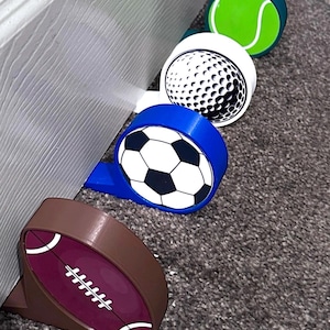 May include: Four door stop stoppers in the shape of sports balls. The door stops are brown, blue, white, and green. The balls are a football, soccer ball, golf ball, and tennis ball.