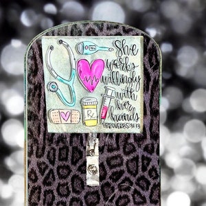 May include: A black and white leopard print background with a clear acrylic badge holder. The badge holder has a pink heart, a stethoscope, a thermometer, a syringe, a bandage, and a prescription bottle. The text on the badge holder reads "She works willingly with her hands" Proverbs 31:13.