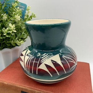 May include: A small, green ceramic vase with a white and red geometric design. The vase has a rounded body and a flared lip.