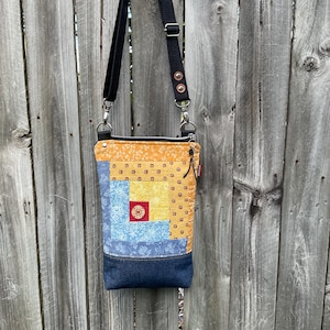 May include: A small yellow, blue and red patchwork fabric crossbody bag with a black adjustable strap. The bag has a denim bottom and a zipper closure.