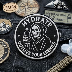Op de afbeelding: Zwart en wit geborduurde patch met een zeisdrager die een waterfles vasthoudt, met de tekst "HYDRATE OUTLIVE YOUR ENEMIES". Extra patches met berg- en kompasontwerpen zijn zichtbaar.