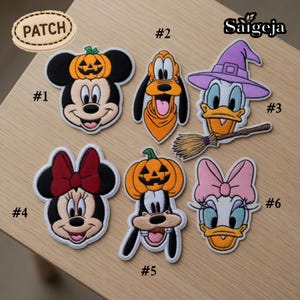 May include: Six embroidered patches featuring cartoon characters: Mickey Mouse with a pumpkin, Pluto, Donald Duck with a witch hat and broom, Minnie Mouse with a red bow, Goofy with a pumpkin, and Daisy Duck with a pink bow. Each patch is numbered.