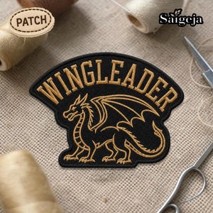 May include: Black embroidered patch with the word "WINGLEADER" in gold lettering. A gold dragon design is centered below the text. The patch is on a textured, neutral-colored surface. A small wooden patch with the word "PATCH" is in the upper left corner.