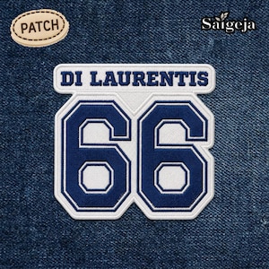Pode incluir: Patch bordado com o texto "DI LAURENTIS" acima do número "66" em azul marinho sobre um fundo branco. Um patch menor com a palavra "PATCH" está no canto superior esquerdo. O fundo é ganga.
