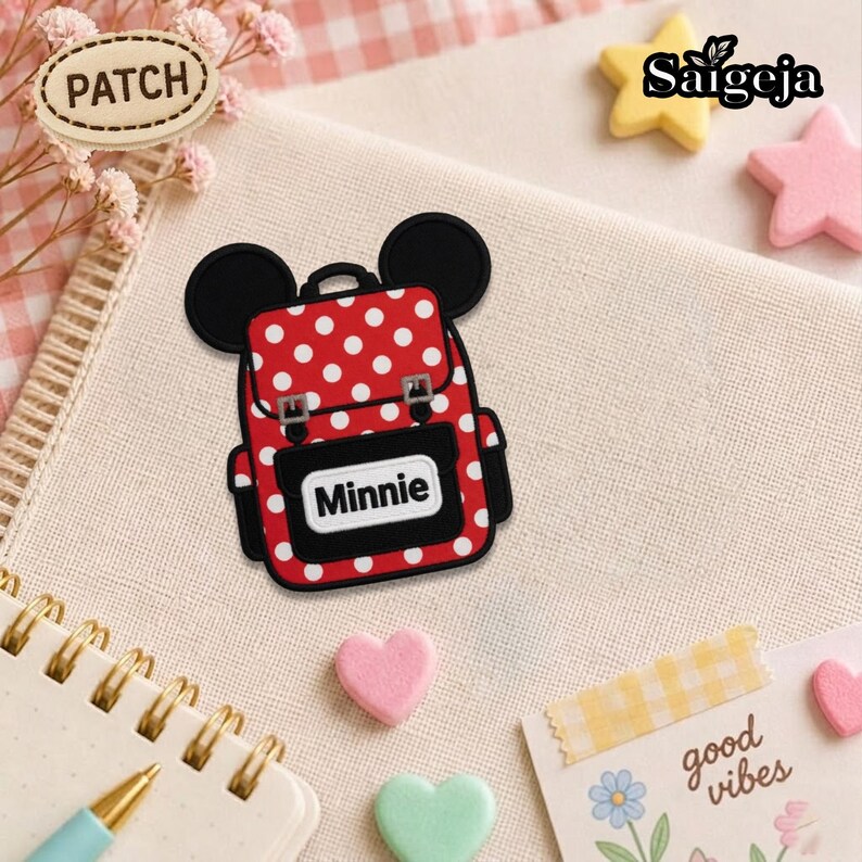 May include: A red and white polka dot backpack patch featuring black mouse ears at the top and a black front pocket with the name Minnie printed in white text. The patch has a black border and two silver-colored buckles on the front flap.