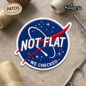 Pode incluir: Patch bordado com fundo azul, texto branco e design vermelho. O texto diz "NOT FLAT - WE CHECKED" em branco. O patch é redondo e tem uma borda branca. O patch está em uma superfície de tecido bege.