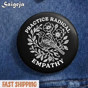 Może przedstawiać: Czarny, okrągły guzik z białym tekstem i wzorem ptaka i kwiatów. Tekst brzmi "PRACTICE RADICAL EMPATHY". Guzik jest umieszczony na tle niebieskiego denimu.