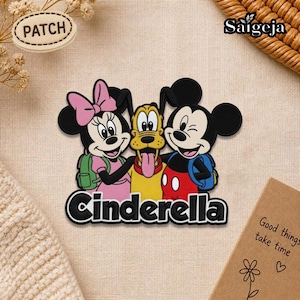 Peut inclure: Un écusson coloré représentant Minnie, Pluto et Mickey Mouse avec le mot "Cinderella" en dessous. Minnie porte un nœud rose et Pluto tire la langue. Mickey fait un clin d'œil. L'écusson est sur fond beige.