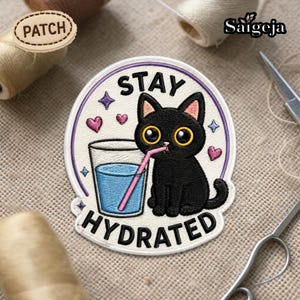 Op de afbeelding: Geborduurde patch met een zwarte kat die uit een glas water met een roze rietje drinkt. De patch heeft de woorden "STAY HYDRATED" en is versierd met hartjes en sterren. De patch is ongeveer 7.6 cm in diameter.