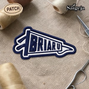 May include: A navy blue and white embroidered patch in a pennant shape, with the word "BRIARU" in white block letters. The patch is bordered with white stitching and is on a tan fabric surface. The word "PATCH" is on a wooden tag.