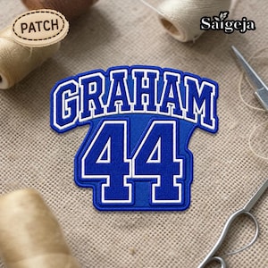 May include: A blue and white embroidered patch with the name "GRAHAM" and the number "44". The patch has a white border and is set against a neutral background. The word "PATCH" is on a small wooden tag.
