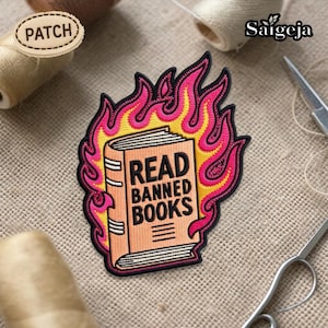 Può includere: Toppa ricamata raffigurante un libro in fiamme, con la scritta "READ BANNED BOOKS". La toppa ha un design a fiamma rosa e gialla e un bordo nero. La toppa è su uno sfondo di tessuto beige. Un articolo a tema libri.