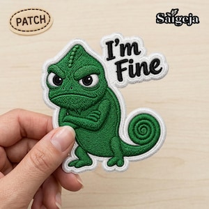 Könnte beinhalten: Ein gestickter Aufnäher mit einem grünen Chamäleon mit mürrischem Gesichtsausdruck und verschränkten Armen. Der Text "I'm Fine" ist in Schwarz über dem Chamäleon gestickt. Der Aufnäher hat einen weißen Rand, der dem Umriss des Motivs folgt.