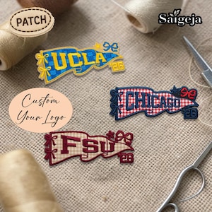 Op de afbeelding: Geborduurde patches met de tekst "UCLA", "CHICAGO" en "FSU". Elke patch heeft een bannerontwerp met strikken en het nummer "26". De patches liggen op een getextureerd, neutraal gekleurd oppervlak.