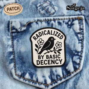 May include: A denim pocket with two patches. One patch is oval and reads "PATCH". The other patch is rectangular with a black bird on a branch, surrounded by flowers, and the words "RADICALIZED BY BASIC DECENCY".