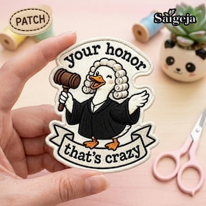 May include: An embroidered patch featuring a white duck dressed as a judge in a black robe and white wig, holding a brown wooden gavel. The text above reads your honour and the text below reads that's crazy, all on a cream-coloured background.