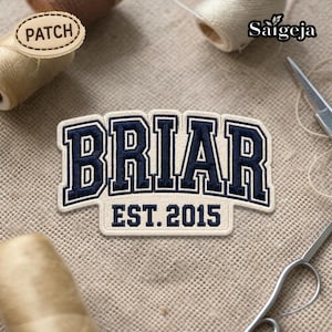 May include: Embroidered patch featuring the word "BRIAR" in navy blue block letters with a white outline, and the text "EST. 2015" below. The patch is on a beige background, with sewing supplies in the background.