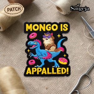 May include: Embroidered patch with the text "MONGO IS APPALLED!" featuring a blue dinosaur with pink accents and a cat wearing sunglasses. The patch includes donut and star graphics, with a black border and yellow text.