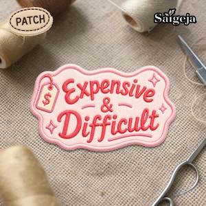 May include: A pink and red embroidered patch with the words "Expensive & Difficult" in a playful font. The patch has a price tag graphic and star accents. The patch is on a textured, neutral background.