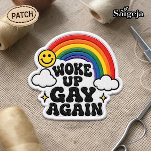 Puede incluir: Parche bordado con un arcoíris, una cara sonriente amarilla y el texto "WOKE UP GAY AGAIN". El parche tiene un borde blanco y está diseñado para coser o planchar sobre ropa o artículos de tela. Un accesorio vibrante y audaz.