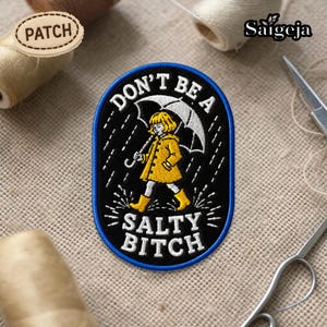May include: Embroidered patch with a black background and a blue border. The patch features a person in a yellow raincoat and boots holding an umbrella in the rain. Text on the patch reads "DON'T BE A SALTY BITCH."