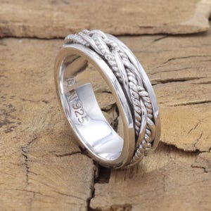 May include: A silver ring with a braided design. The ring is marked with "925" on the inside.