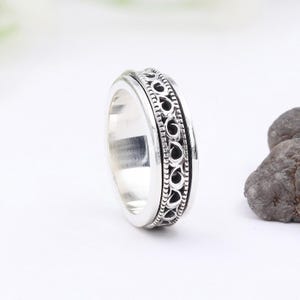 May include: A silver spinning ring with a decorative design. The ring is made of metal and has a smooth finish.