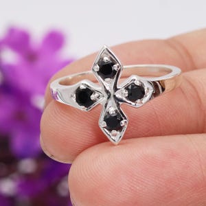 May include: A silver ring with a cross design featuring four black gemstones.