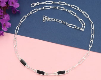 Può includere: Una collana a catena d'argento con accenti di pietre preziose nere rettangolari. La collana presenta un delicato design a catena con chiusura a moschettone. Le pietre preziose sono uniformemente distanziate, creando un look moderno ed elegante.