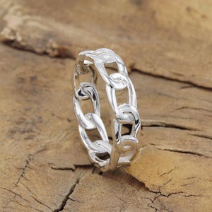 Puede incluir: Un anillo de plata con diseño de cadena. El anillo está hecho de un solo diseño de cadena continuo.