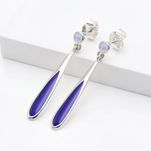 May include: A pair of silver dangle earrings with a blue enamel drop and a moonstone accent.
